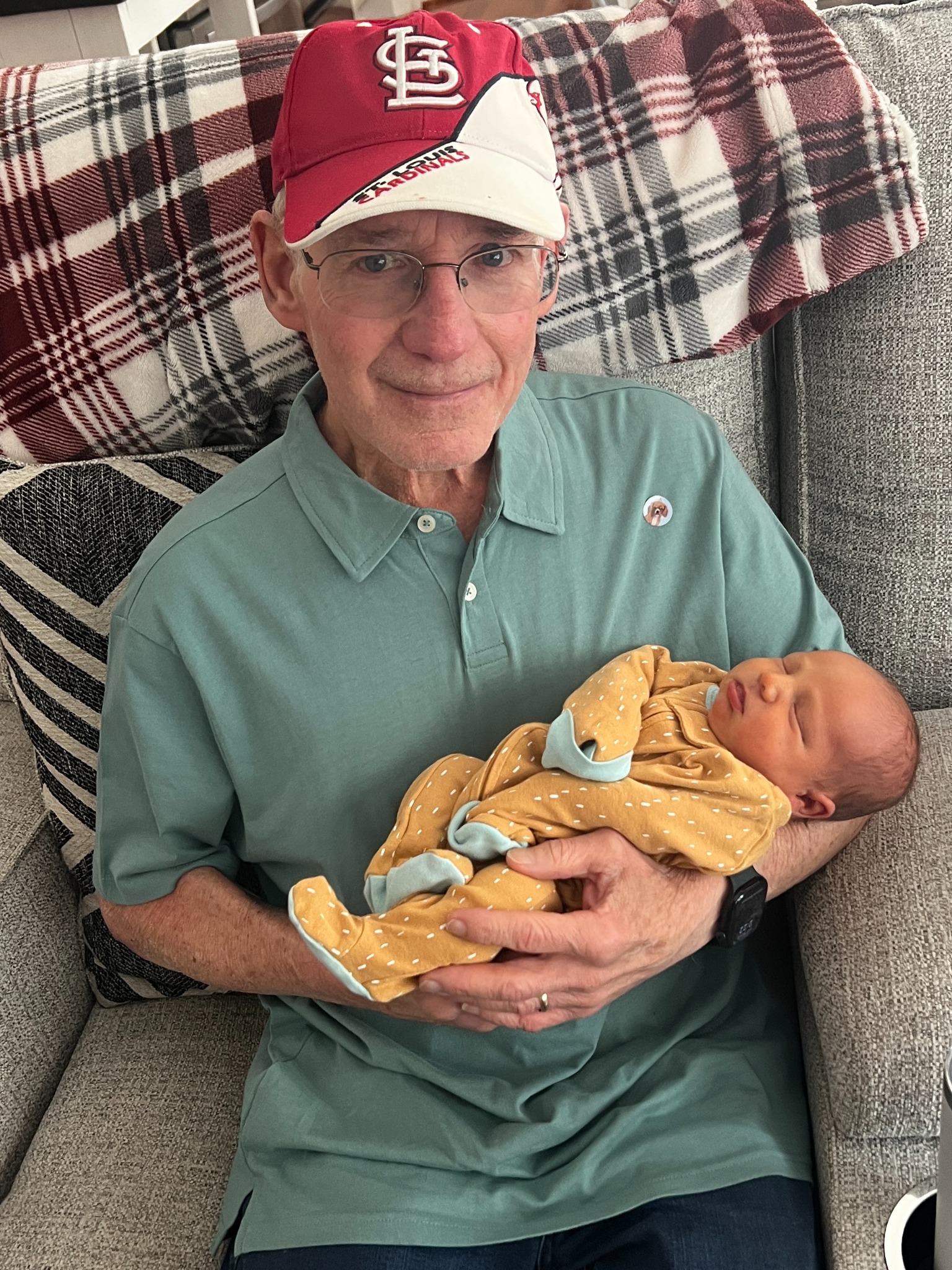 A grandfather in a Cardinals cap holding a sleeping baby